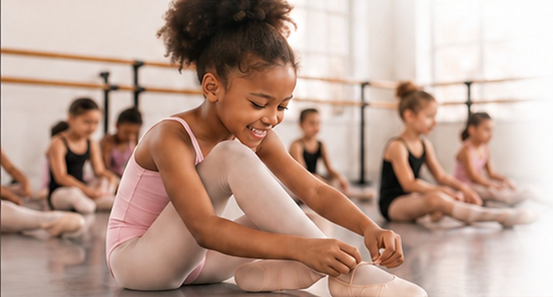 A young dancer smiling as she ties her ballet slippers on the studio floor